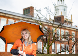 Female student stands with umbrella in front of Rockwell Hall